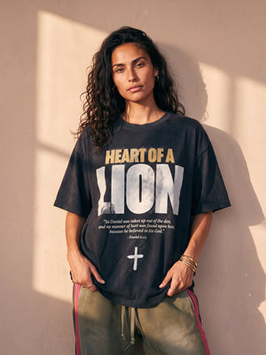 Heart of a Lion faded black tee, front print, woman with long curly hair and hands at her hem, worn with striped track pants