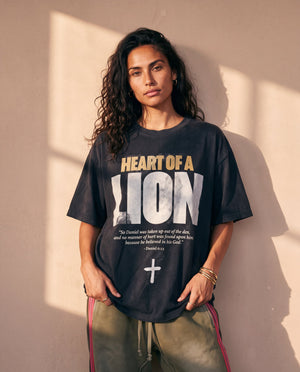Heart of a Lion faded black tee, front print, woman with long curly hair and hands at her hem, worn with striped track pants