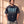 Pray Until Something Happens faded black tee, front print, man with curly hair and hands in his pockets, styled with ripped camo cargo pants