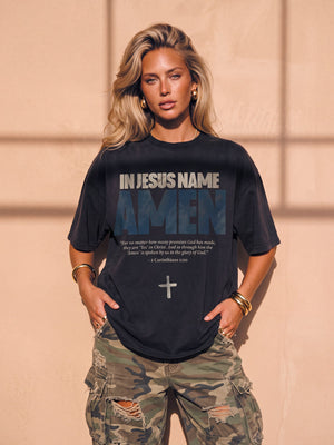In Jesus Name Amen faded black tee, front print, woman with long wavy hair and hoop earrings, hands in her ripped camo cargo pants