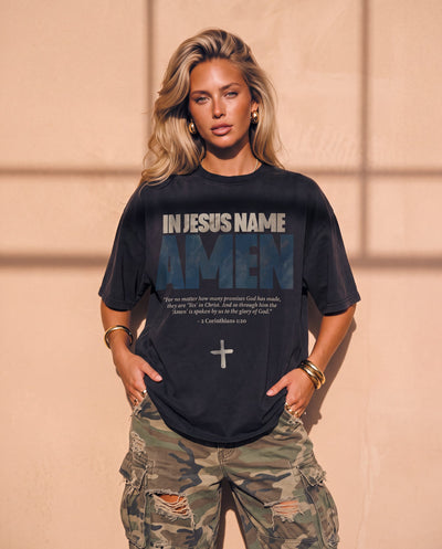 In Jesus Name Amen faded black tee, front print, woman with long wavy hair and hoop earrings, hands in her ripped camo cargo pants