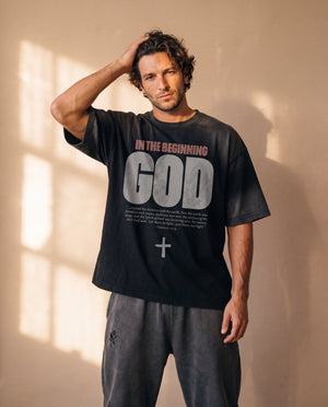In the Beginning God faded black tee, man with a hand in his hair, thigh up, drop shoulders and the Genesis 1:1–5 verse in focus