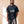 Jesus Is King faded black tee, front print, man with braided hair looking to the side, hands relaxed in warm window light