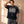 In the Beginning God faded black tee, front print, worn by a man running one hand through his hair against a sunlit wall