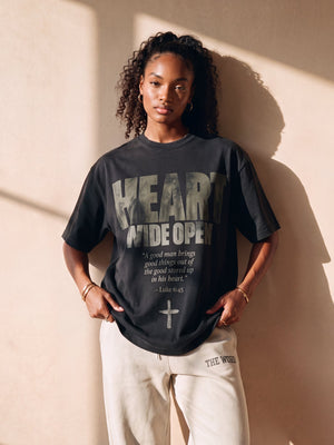 Heart Wide Open faded black tee, front print, woman with curly hair holding the hem, worn with THE WORD sweatpants