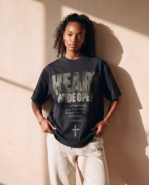 Heart Wide Open faded black tee, front print, woman with curly hair holding the hem, worn with THE WORD sweatpants