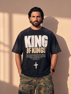 King of Kings faded black tee, front print, bearded man with hands in his pockets and camo cargo pants against a sunlit wall