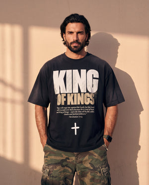 King of Kings faded black tee, front print, bearded man with hands in his pockets and camo cargo pants against a sunlit wall