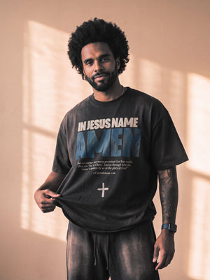 In Jesus Name Amen faded black tee, front print, man with an afro and a beard pulling the hem, worn with THE WORD sweatpants