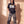 Daughter of the King faded black tee, full body view of a woman in washed cargo pants and sneakers, one hand in her pocket by a sunlit wall