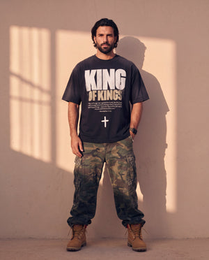 King of Kings faded black tee, full body view of a bearded man in camo cargo pants and work boots, Christian streetwear look