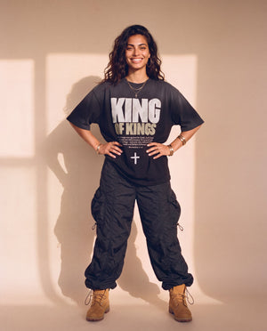 King of Kings faded black tee, full body view of a smiling woman with hands on her hips in cargo pants and work boots