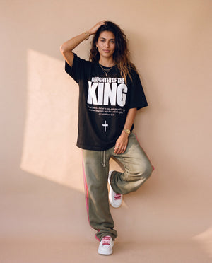 Daughter of the King tee, black, front print, woman, leaning on wall full body