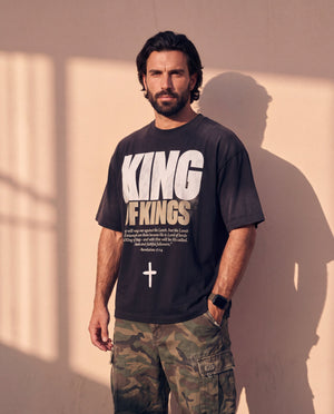 King of Kings faded black tee, three quarter view of a bearded man with one hand in his pocket and the oversized fit hanging loose