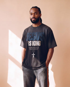 Jesus Is King faded black tee, front print, bearded man with hands in his pockets, John 1:1 verse under JESUS IS KING