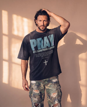 Pray Until Something Happens faded black tee, man with a hand in his hair, thigh up, the John 14:13–14 verse and cross in view