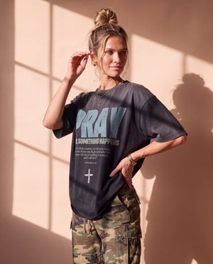 Pray Until Something Happens faded black tee, three quarter angle on a woman with a hand by her hair and one on her hip, boxy fit