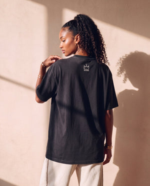 Heart Wide Open faded black tee, back view of a woman with a curly ponytail touching her shoulder, crown logo below the collar