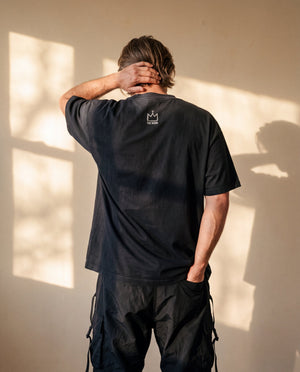 Heart of a Lion faded black tee, back view of a man with a hand behind his head, small crown logo below the collar