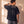 In the Beginning God faded black tee, back view of a man with a hand on his neck, showing the boxy cut and small crown logo