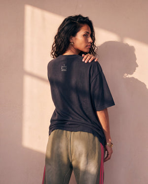 Heart of a Lion faded black tee, back view of a woman with a hand on her shoulder looking aside, crown logo below the collar