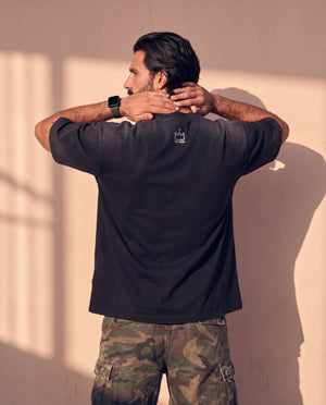 King of Kings faded black tee, back view of a man with both hands behind his head, crown logo centred below the collar
