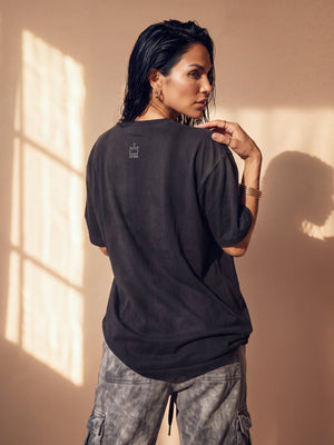 Daughter of the King faded black tee, back view of a woman with a hand on her shoulder, small crown logo below the collar