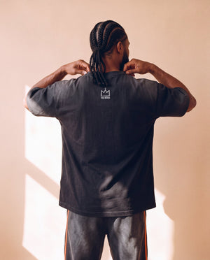 Jesus Is King faded black tee, back view of a man with braids holding the collar, crown logo centred under the neckline