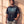 Pray Until Something Happens faded black tee, front print, man leaning on a sunlit wall with one hand in his pocket and his gaze to the side
