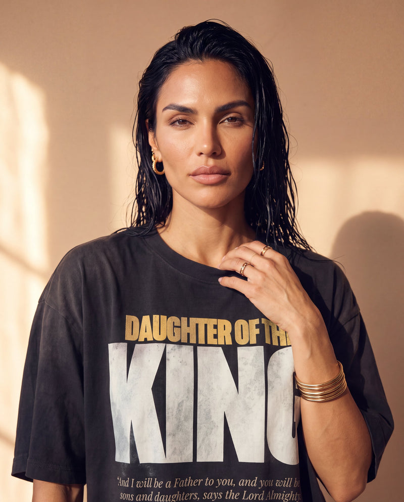 Daughter of the King faded black tee, close up portrait of a woman with a hand at the collar above the DAUGHTER OF THE KING lettering