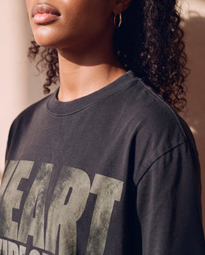 Heart Wide Open faded black tee, close up of a woman's neckline and dropped shoulder, the distressed HEART lettering below