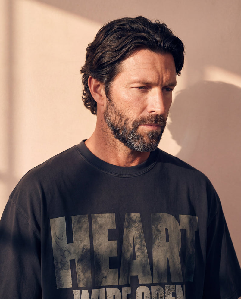Heart Wide Open faded black tee, close up portrait of a man with a beard looking down above the large HEART lettering