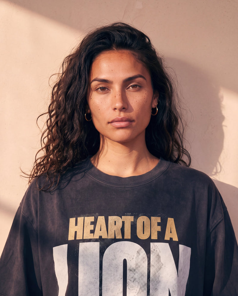 Heart of a Lion faded black tee, close up portrait of a woman with curly hair above the HEART OF A LION lettering