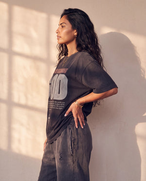 In the Beginning God faded black tee, side profile of a woman with a hand on her hip, showing the dropped shoulder and relaxed length