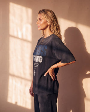 Jesus Is King faded black tee, side profile of a woman with a hand on her hip, showing the relaxed length and boxy oversized cut