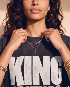 King of Kings faded black tee, close up of a woman holding the ribbed collar, cross necklace and hoop earrings above KING