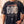 In the Beginning God faded black tee, front print close crop on a man with a hand in his pocket, the full verse and cross in frame