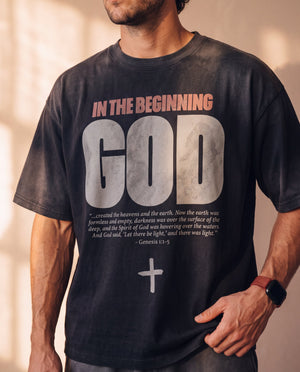 In the Beginning God faded black tee, front print close crop on a man with a hand in his pocket, the full verse and cross in frame