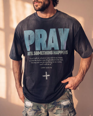 Pray Until Something Happens faded black tee, front print close crop on a man with a hand on his hip, the full John 14:13–14 verse and cross