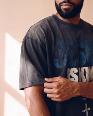 Jesus Is King faded black tee, close up on a man's sleeve and chest, distressed JESUS IS KING lettering and the dropped shoulder seam