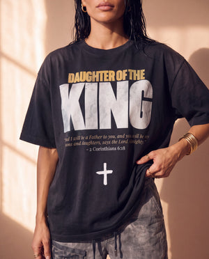 Daughter of the King faded black tee, front print close crop on a woman holding the hem, the verse and cross, Christian streetwear