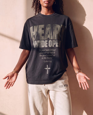 Heart Wide Open faded black tee, front print, woman with open palms at her sides, boxy fit with the full verse and cross