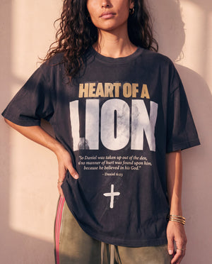 Heart of a Lion faded black tee, front print close crop on a woman with a hand on her hip, the Daniel 6:23 verse and cross in full