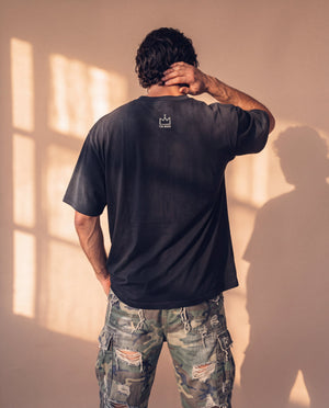Pray Until Something Happens faded black tee, back view of a man with a hand on the side of his neck, small crown logo below the collar