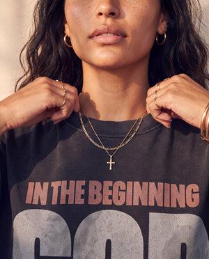 In the Beginning God faded black tee, close up of a woman holding the ribbed collar, cross necklace above the In the Beginning lettering