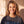 Jesus Is King faded black tee, close up portrait of a smiling woman with wavy hair and a cross necklace above the JESUS lettering