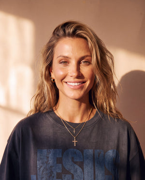 Jesus Is King faded black tee, close up portrait of a smiling woman with wavy hair and a cross necklace above the JESUS lettering