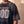 In the Beginning God faded black tee, close up on a man's shoulder and chest, the Genesis 1:1–5 verse and cross printed below GOD
