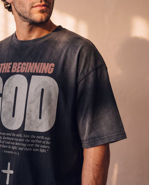 In the Beginning God faded black tee, close up on a man's shoulder and chest, the Genesis 1:1–5 verse and cross printed below GOD