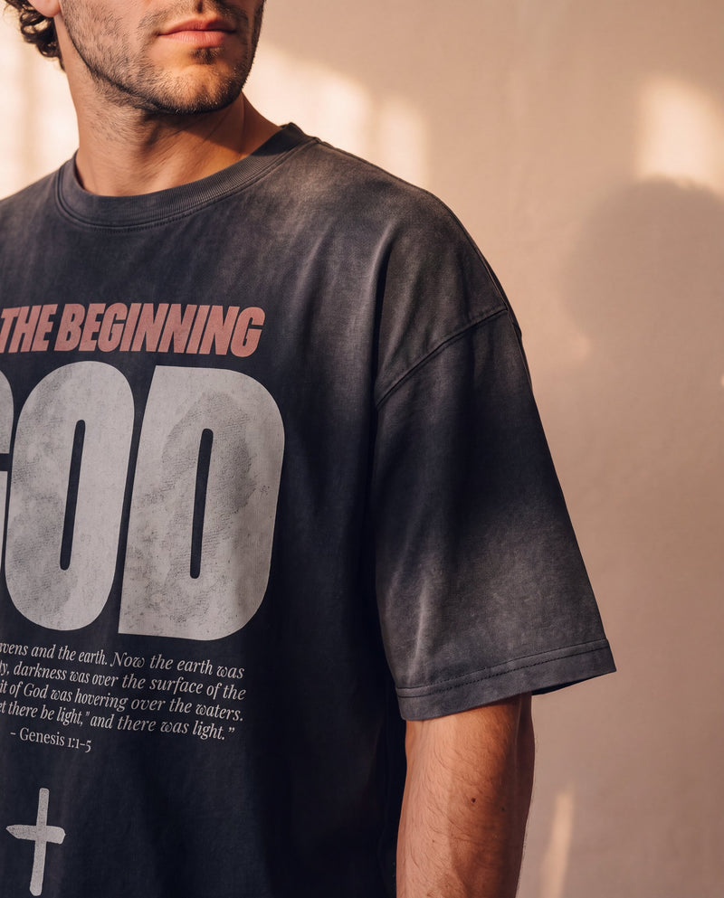 In the Beginning God faded black tee, close up on a man's shoulder and chest, the Genesis 1:1–5 verse and cross printed below GOD